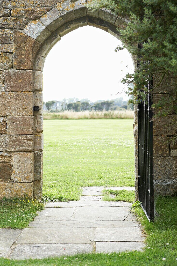 View through paved stone archway with gate to grass field
