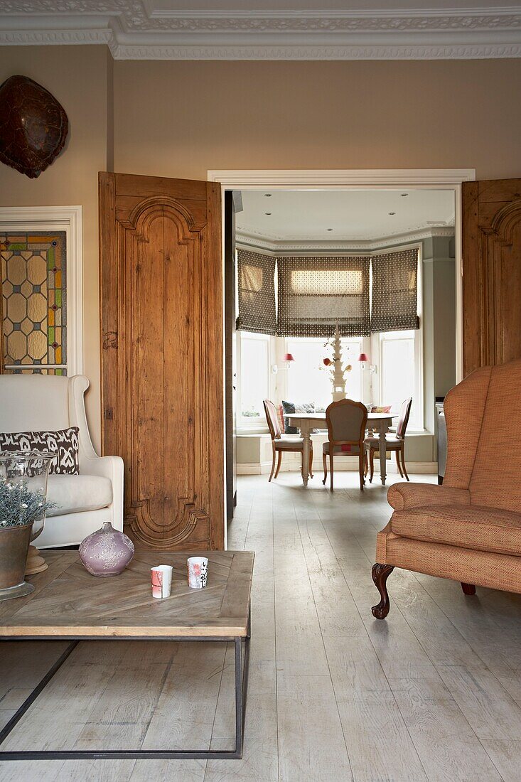 Armchairs and coffee table with view through salvaged double doors to dining room in London home   UK