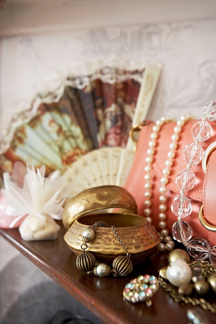 Handbag and jewellery with fan on wooden shelf in London home   UK