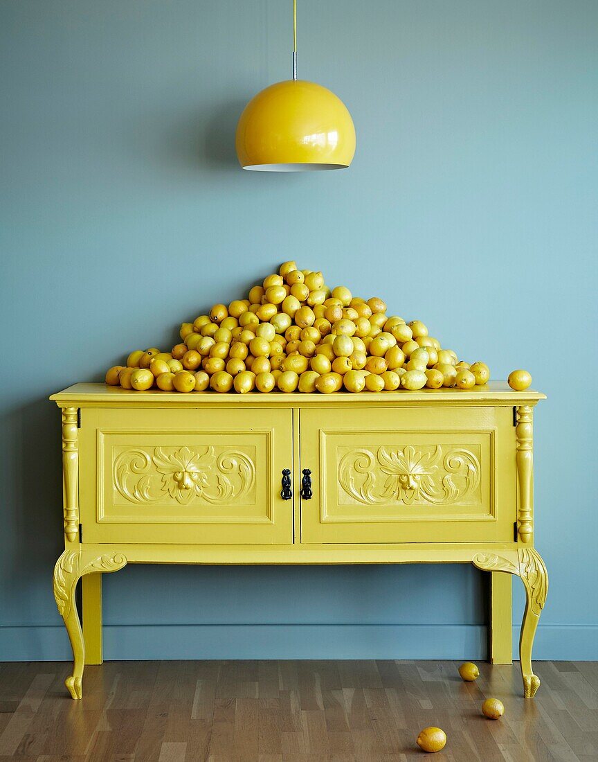 Stack of lemons on painted sideboard with pendant light in turquoise room