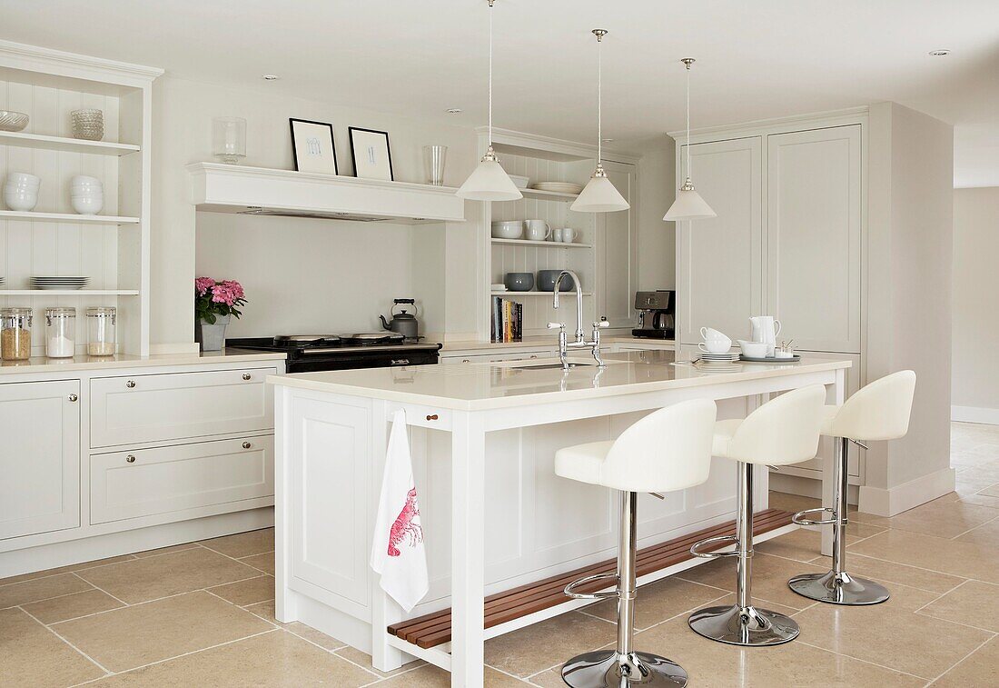 Bar stools at breakfast bar in tiled white kitchen