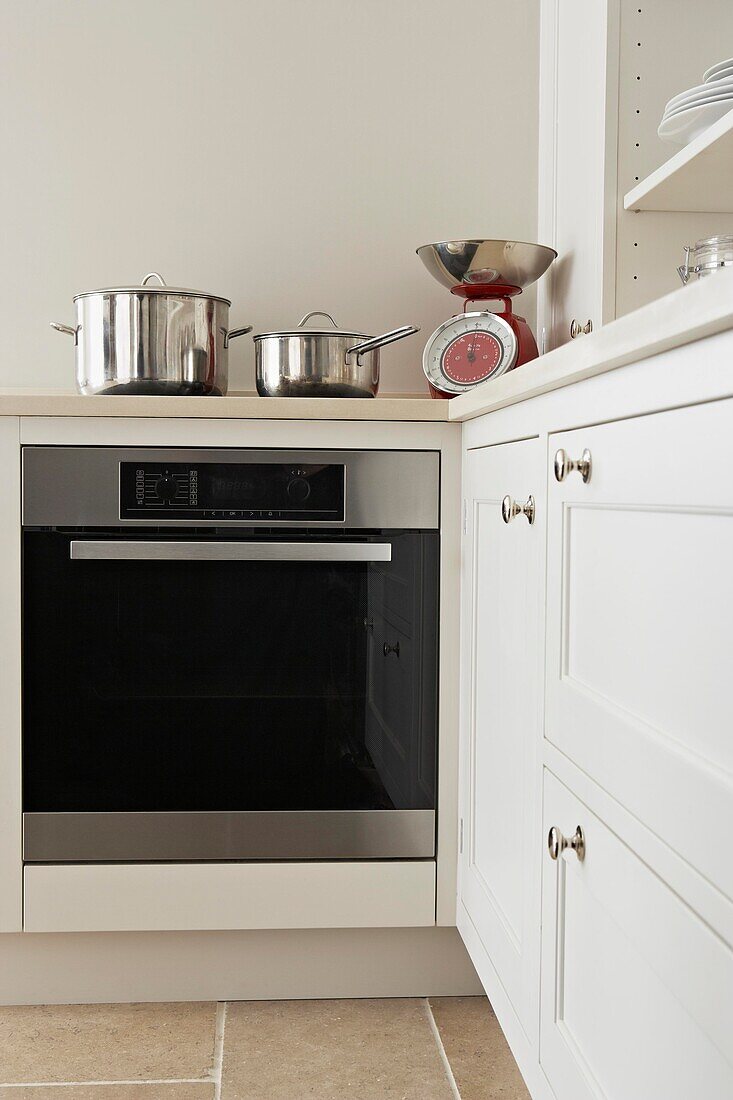 Metal saucepans and kitchen scales with black oven in white fitted kitchen