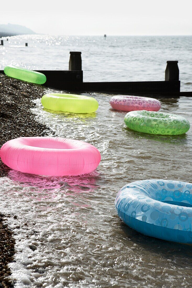 View of pebble beach with 6 multi coloured rubber rings floating with sea groin and horizon