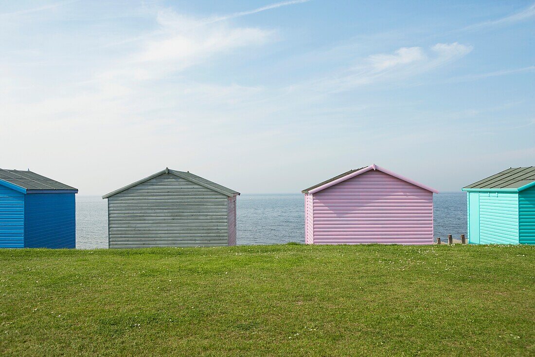 Vier bunte Strandhütten in einer Reihe in Whitstable in Kent mit blauem Himmel und Meerblick