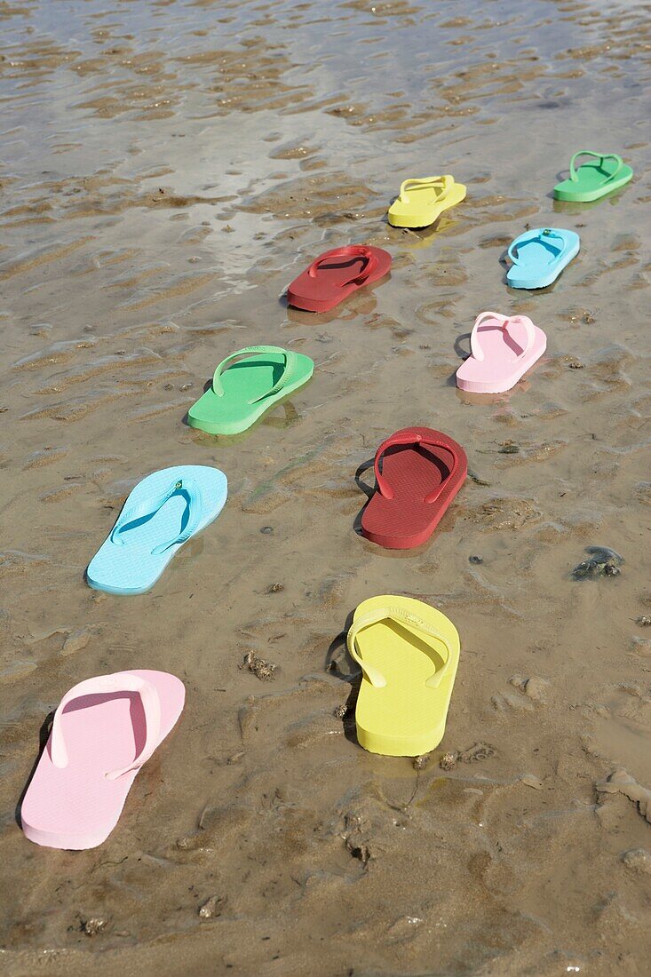 Mehrfarbige Plastik-Flip-Flops in einer Reihe an einem nassen Sandstrand