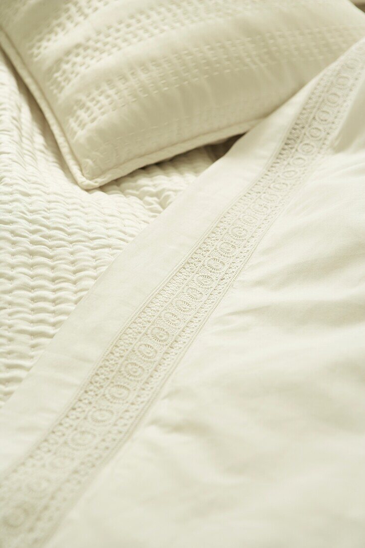 Knusprige weiße Bettwäsche mit Stickerei und Spitze auf einem Bett