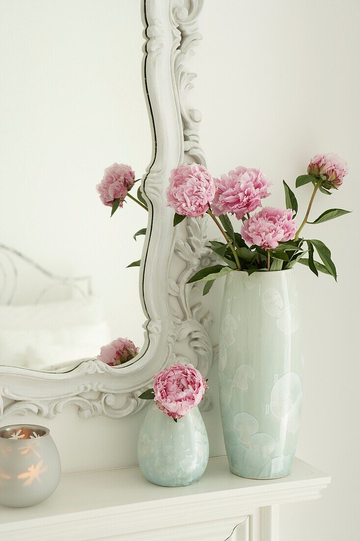 Rosa Pfingstrosen in zwei Vasen neben einem verzierten Spiegelrahmen
