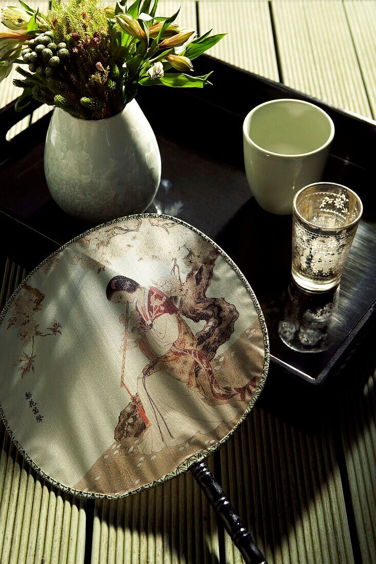 Black tray with Chinese painted silk fan and vase of flowers and tumblers