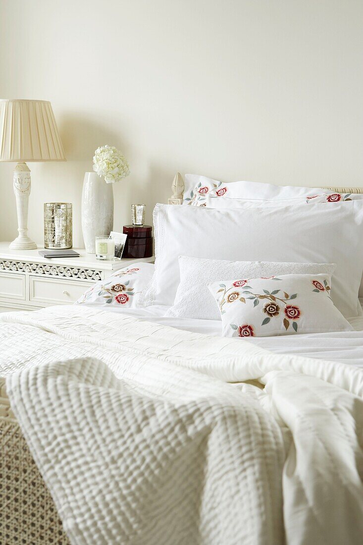 Bett mit weißer Bettwäsche und gestickten Blumenkissen mit Nachttisch