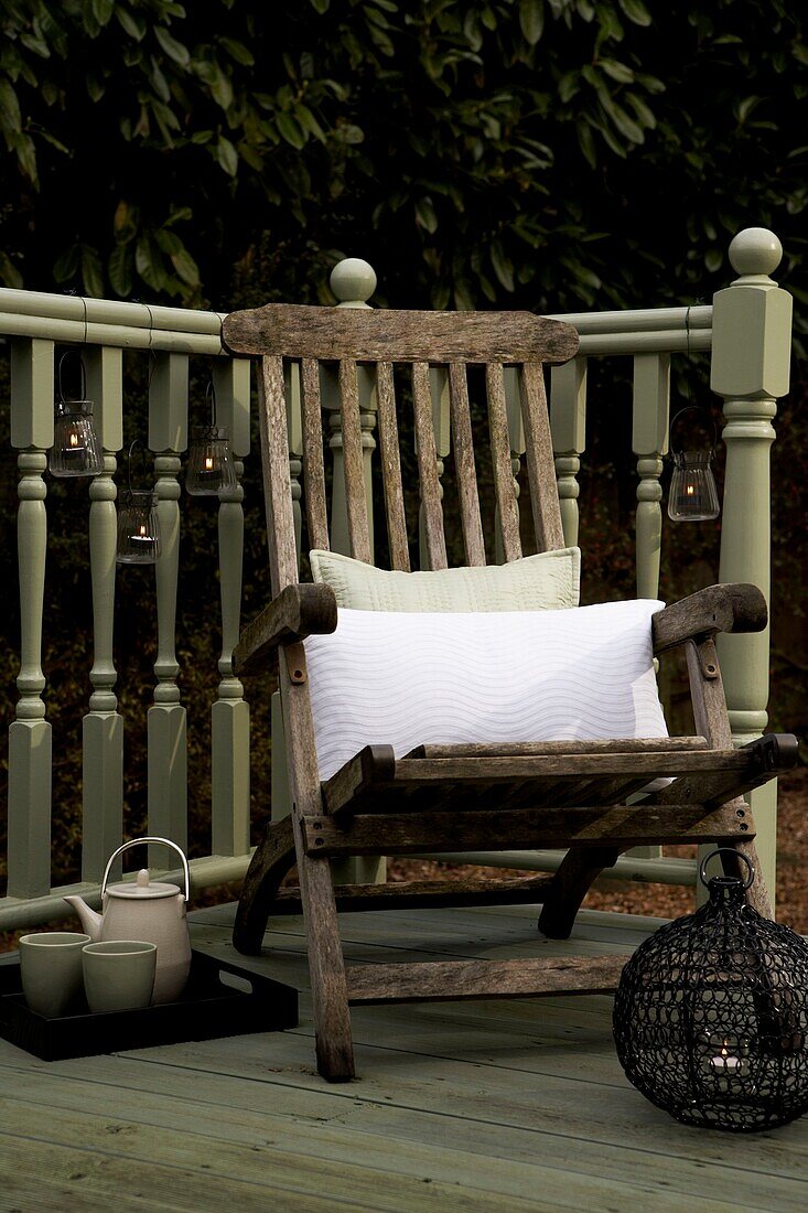 Wooden armchair with cushions on decked garden area with turned ballustrade
