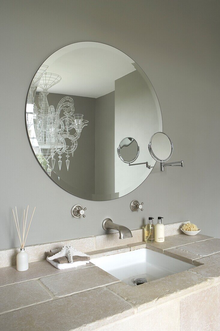 Nahaufnahme eines Waschbeckens mit gefliester Arbeitsplatte und rundem Spiegel