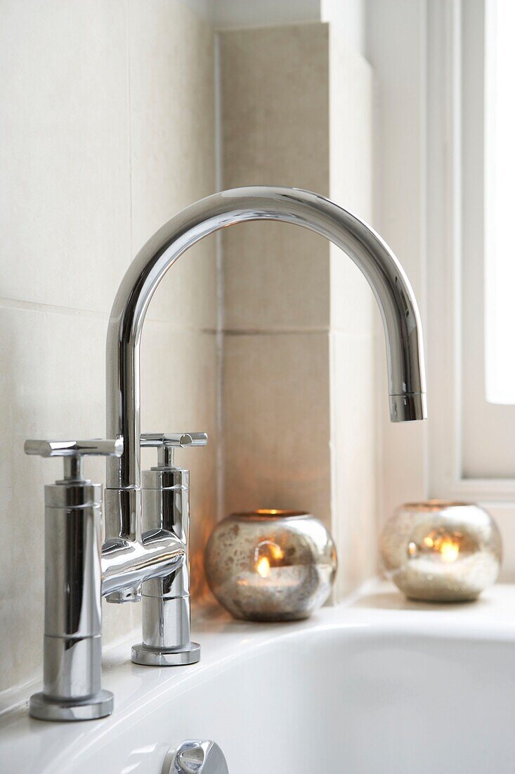 Close up of mixer tap in bathroom with candles burning on bath ledge
