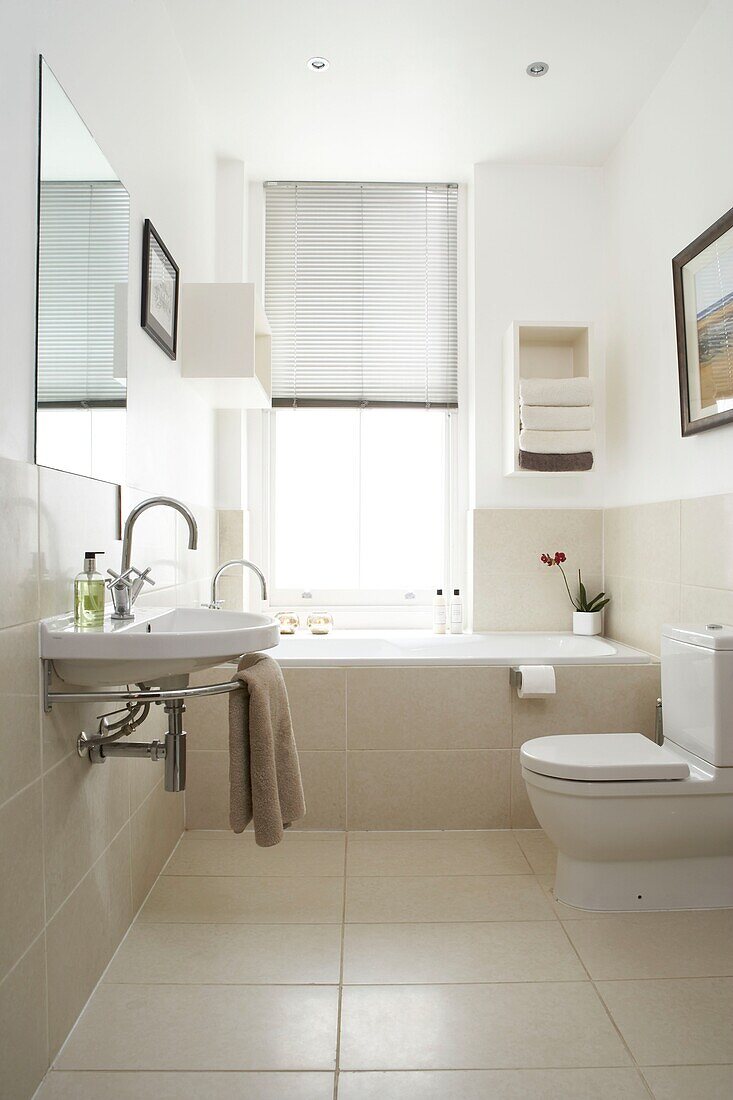 Neutrale Wand- und Bodenfliesen aus Stein in einem hellen Badezimmer mit modernen Accessoires und Toilettenartikeln