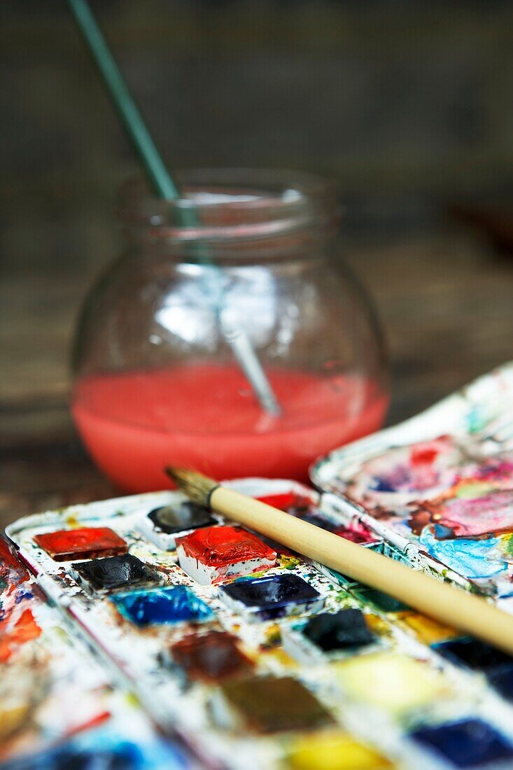 Close up of watercolour palette and paintbrush in water pot