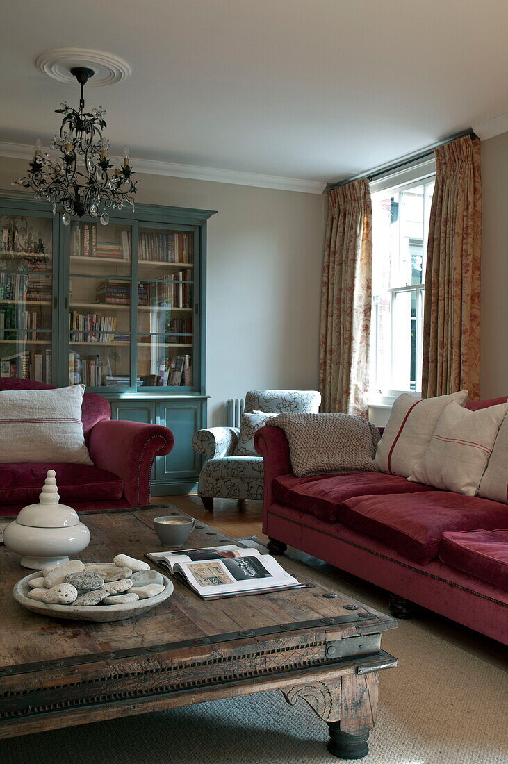 Low wooden coffee table with red velvet sofa and armchair in living room of contemporary Haywards Heath home,  West Sussex,  England,  UK
