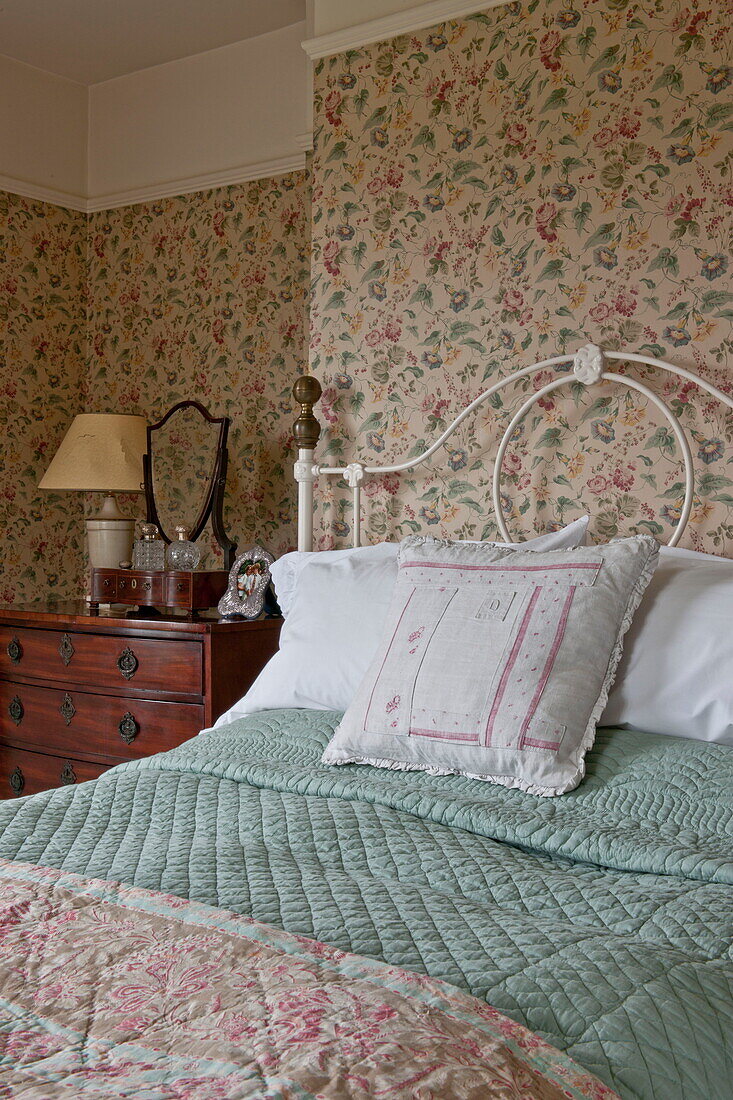 Lace pillow on double bed with green quilt in room with patterned wallpaper,  Ashford home,  Kent,  England,  UK
