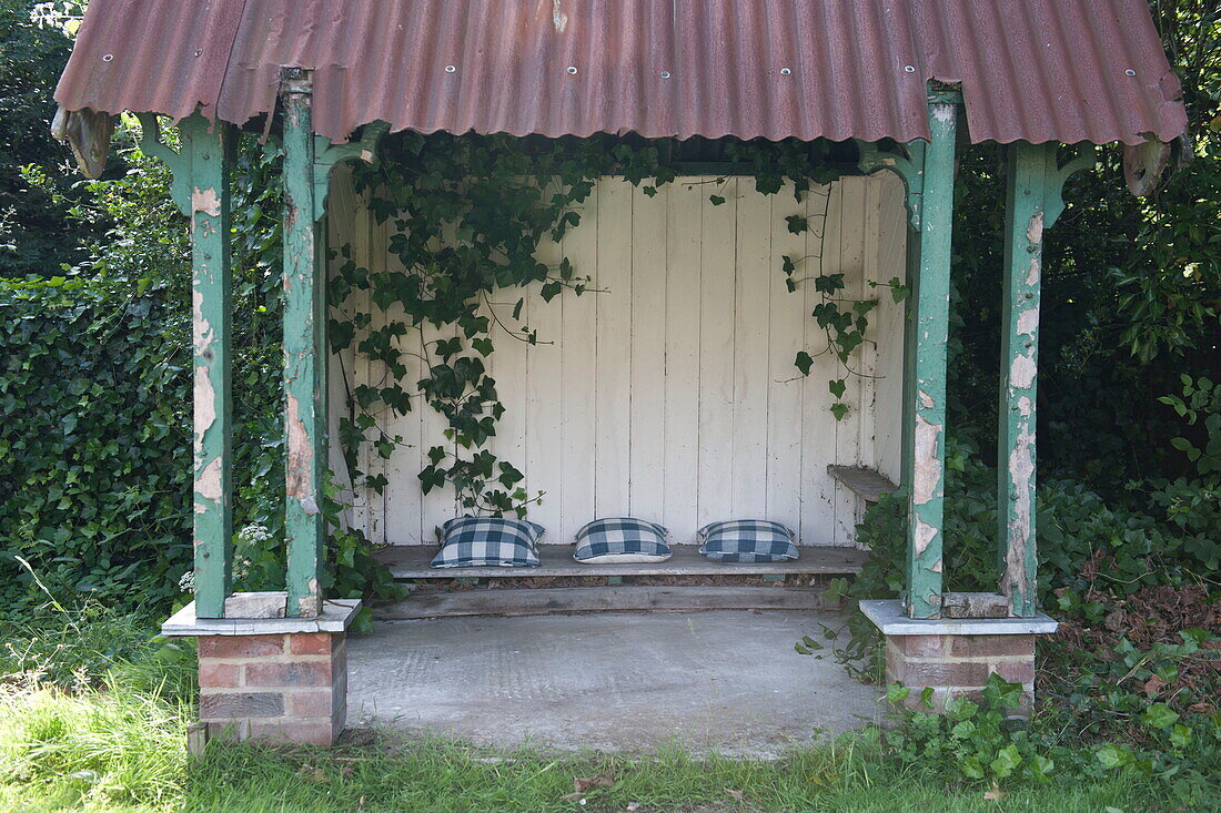Climbing ivy with checked cushions in garden structure,  Ashford,  Kent,  England,  UK