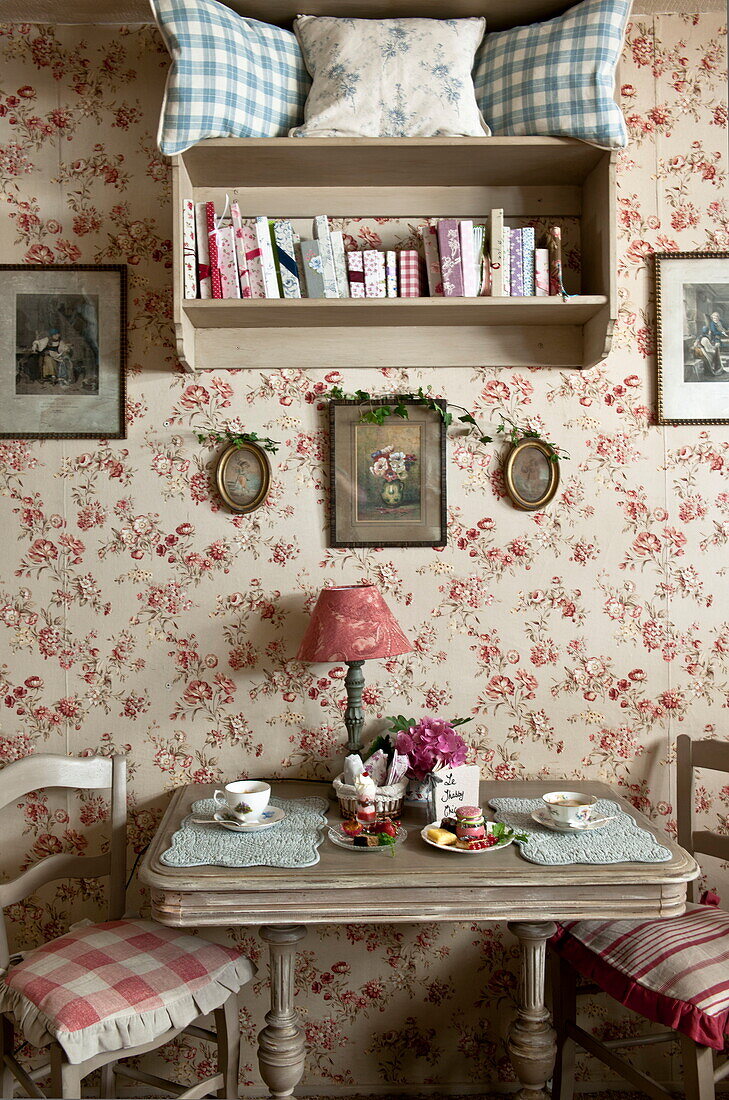 Blumentapete und wandmontiertes Bücherregal über dem Tisch im Teesalon, Dordogne, Frankreich
