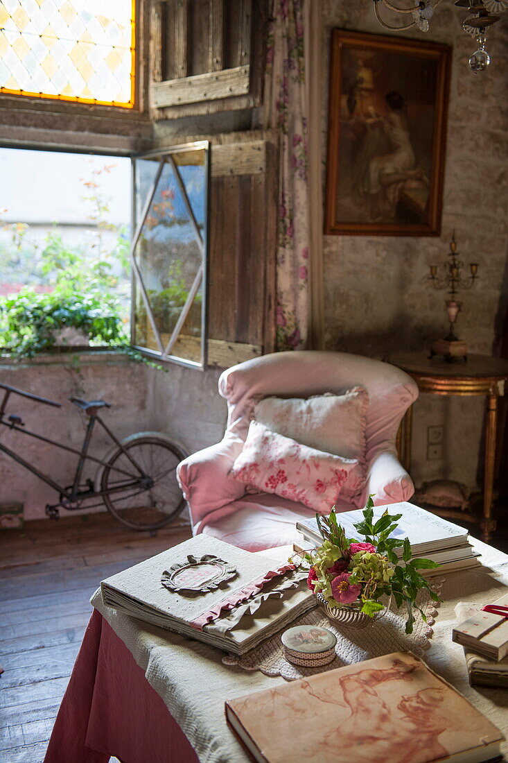 Rosa Sessel mit Fahrrad am offenen Fenster im Wohnzimmer eines Bauernhauses aus Stein, Dordogne, Frankreich