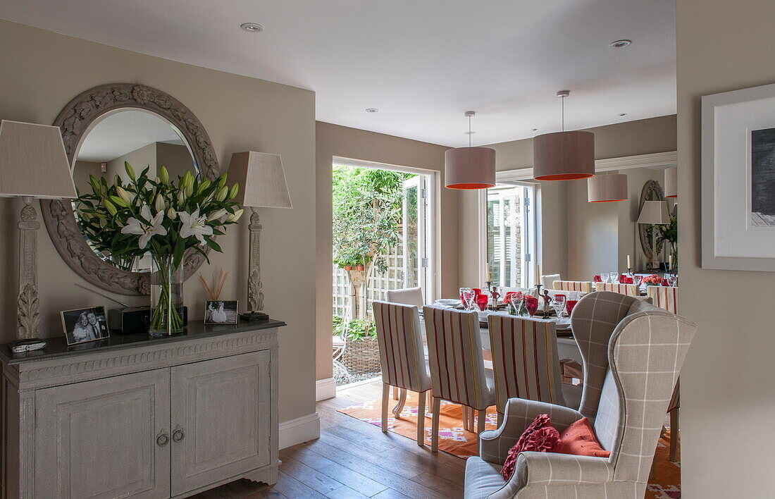 Open plan dining room with large circular mirror over sideboard with cut lilies in Battersea home,  London,  England,  UK