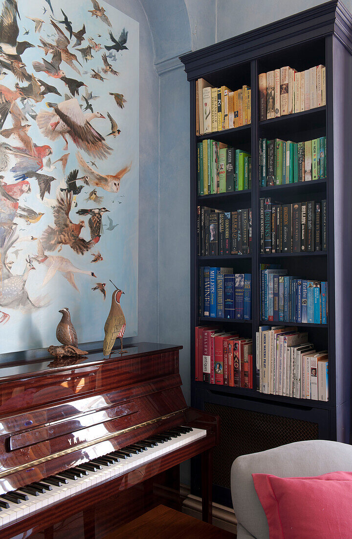 Klavier und Bücherregal mit Wandposter von Vögeln in einem Landhaus in Tiverton, Devon, England, UK