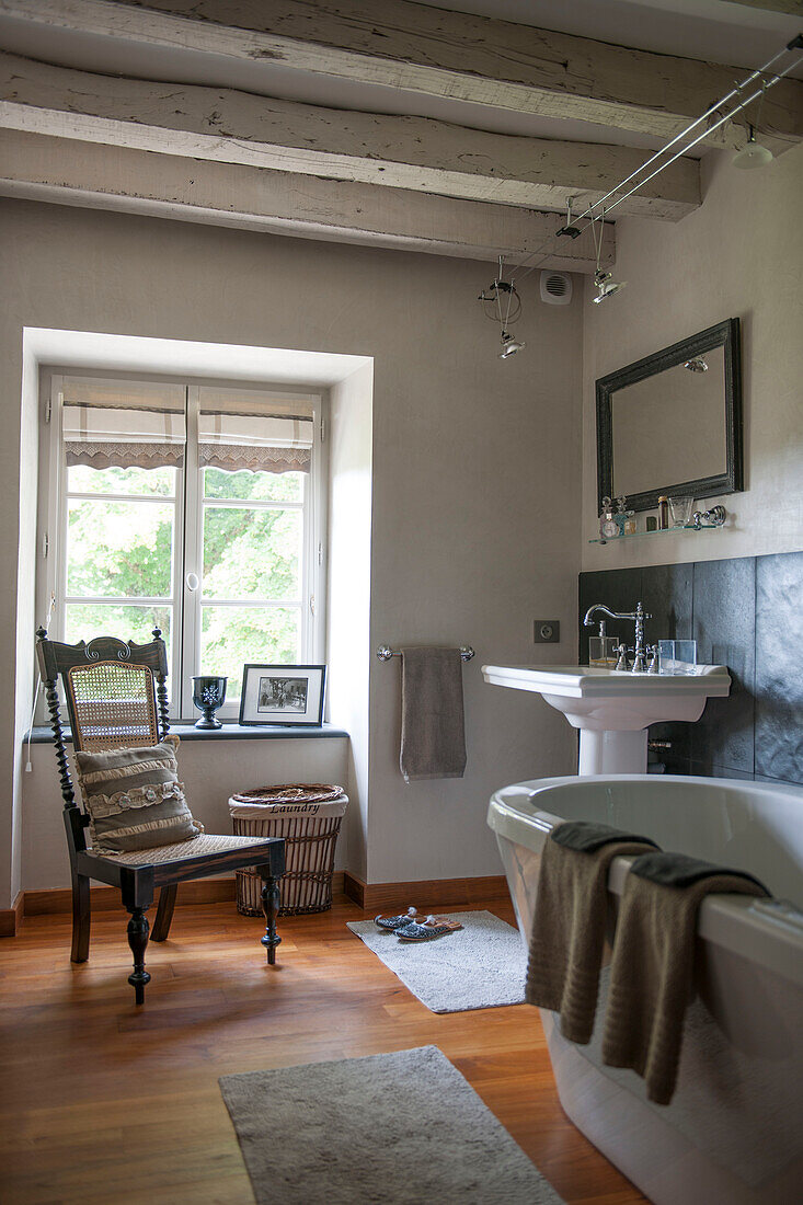 Stuhl am Fenster mit Waschbecken und freistehender Badewanne in einem Bauernhaus in der Dordogne in Perigueux, Frankreich