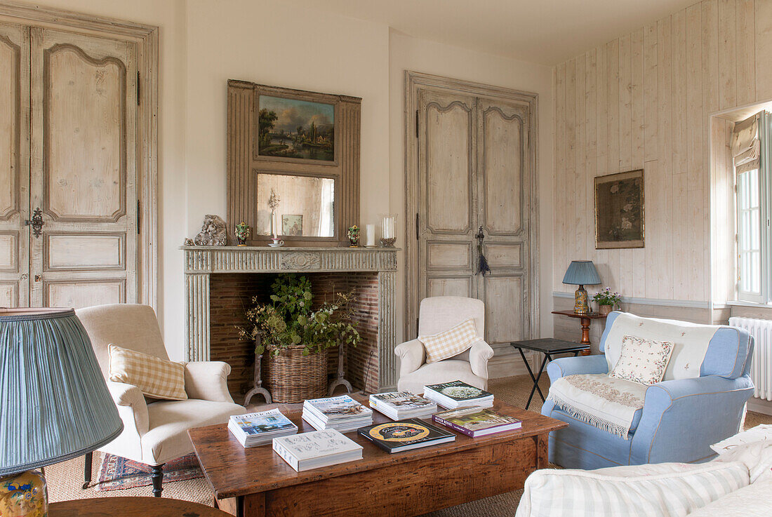 Pastel armchairs at wooden coffee table with double doors in living room of Dordogne cottage  Perigueux  France