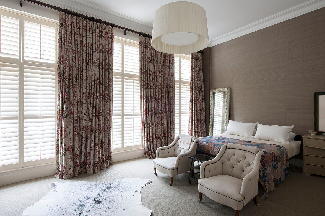 Zwei geknöpfte Sessel mit langen Vorhängen in einem mit Fensterläden versehenen Schlafzimmer in einem Stadthaus in South Kensington London UK