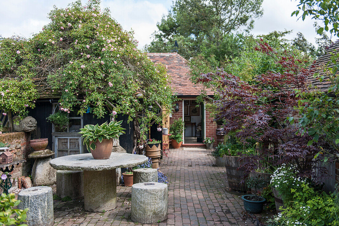 Kletterpflanze mit rustikalem Tisch und Hockern im Backstein-Hinterhof eines Ashford-Bauernhauses in Kent, Großbritannien