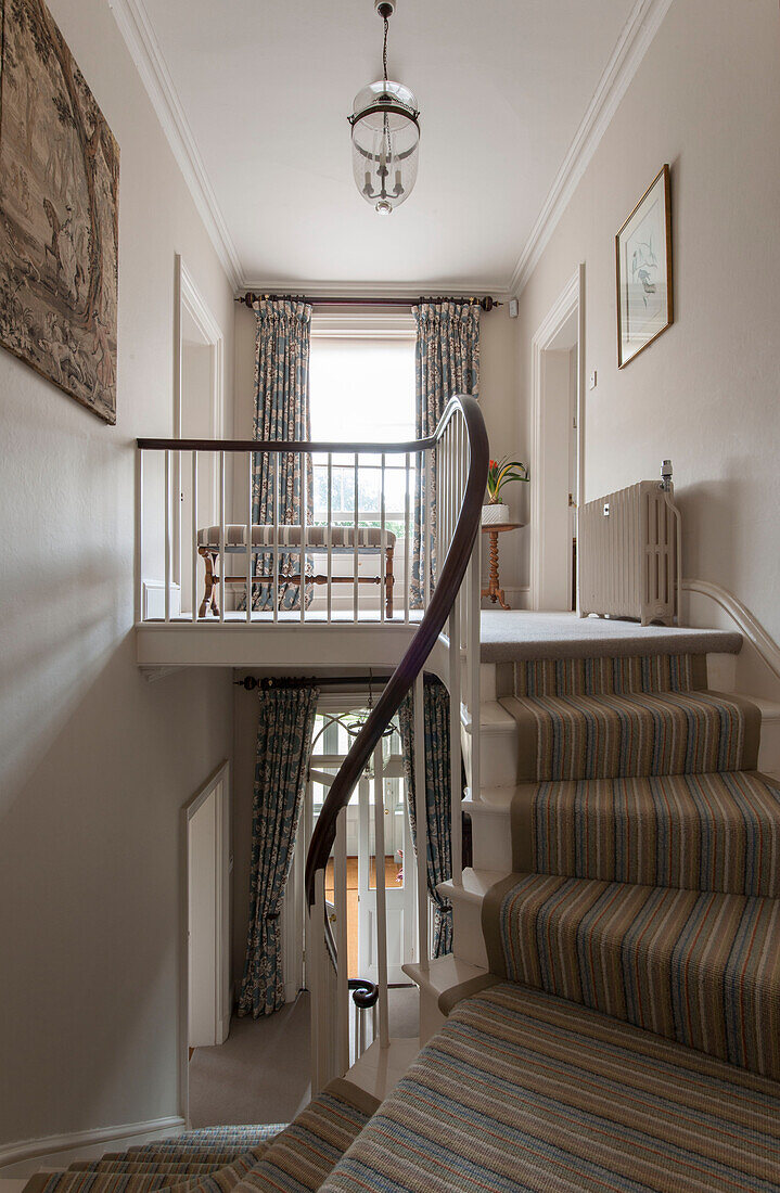 View from staircase to landing and hall with striped carpet runner