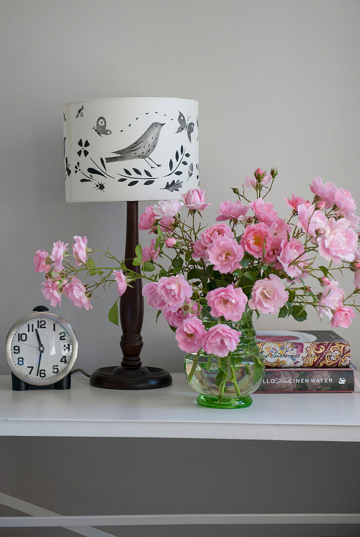 Wecker und rosa Rosen mit Lampe und Büchern auf dem Nachttisch in einem Haus in Kent, England, Vereinigtes Königreich