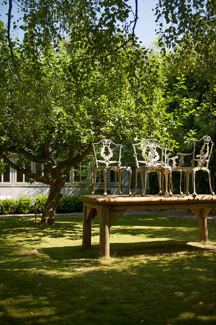 Vintage-Holzstühle auf Holztisch mit Obstbaum im sonnenbeschienenen Garten eines Hauses in Kent England uk