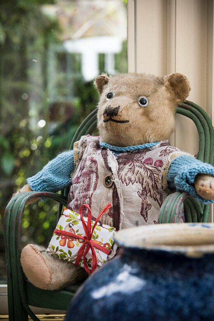 Teddybär auf einem Stuhl im Fenster eines Kutschenhauses in East Sussex, England, Vereinigtes Königreich