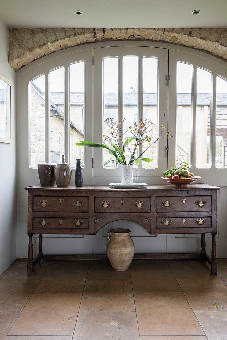 Antique wooden sideboard at arched window in Oxfordshire barn conversion  England  UK