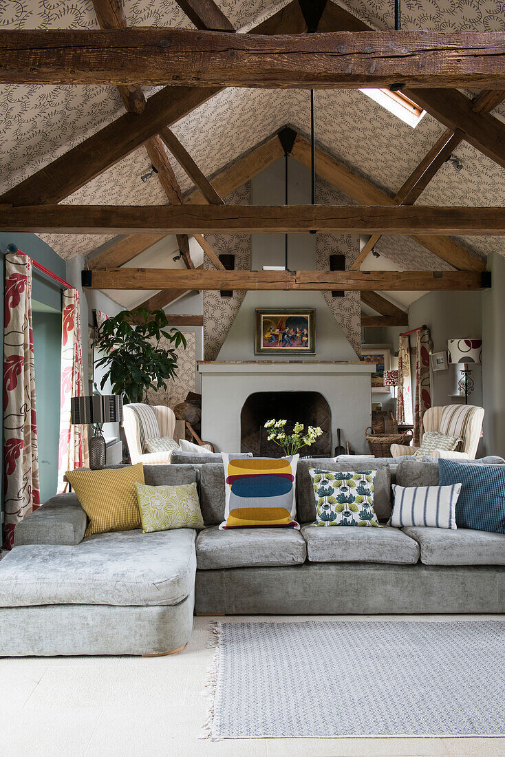 Hellgraues Sofa mit Kissen in einer umgebauten Scheune in Oxfordshire mit tapezierter Decke England UK