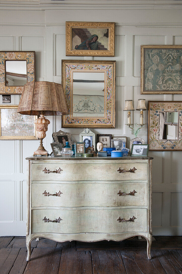 Framed artwork and mirrors with antique chest of drawers in Suffolk home  England  UK