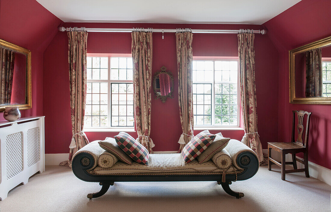Antikes Tagesbett mit karierten Kissen in rotem Schlafzimmer in einem Bauernhaus in Suffolk England UK