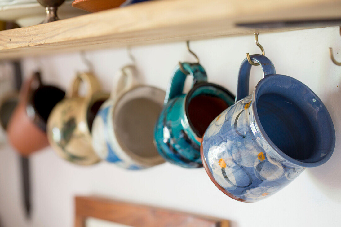 Sortierte Tassen hängen auf einem Regal in einer Küche in Devon England UK