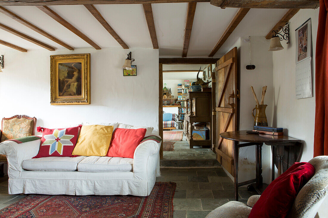 Gilt framed artwork above white sofa with bright cushions in beamed Devon cottage England UK