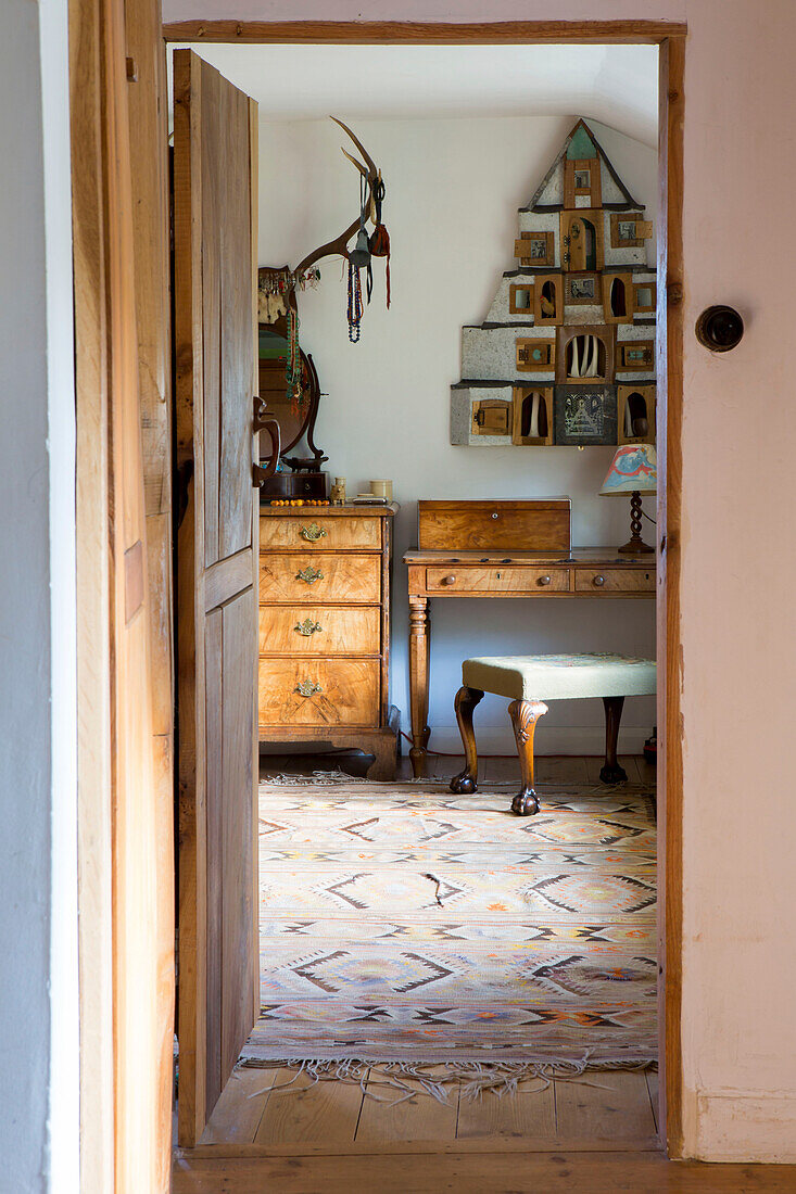 Lagerregal über dem Schreibtisch in einem Raum mit gemustertem Teppich in einem Cottage in Devon, England, UK