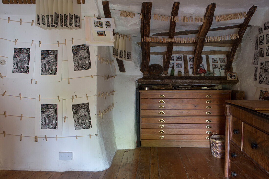 Black and white screenprints hang above wooden chest of drawers in Devon cottage England UK