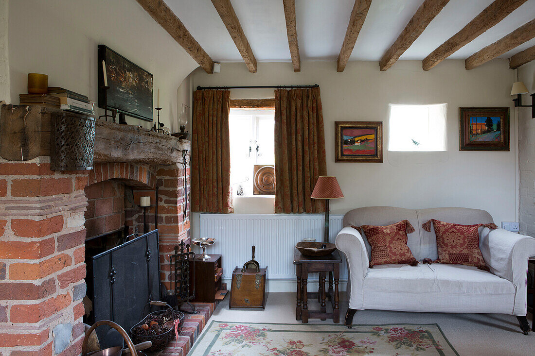 Zweisitzer-Sofa am gemauerten Kamin in einem Cottage mit Balken in Amberley, West Sussex, Großbritannien