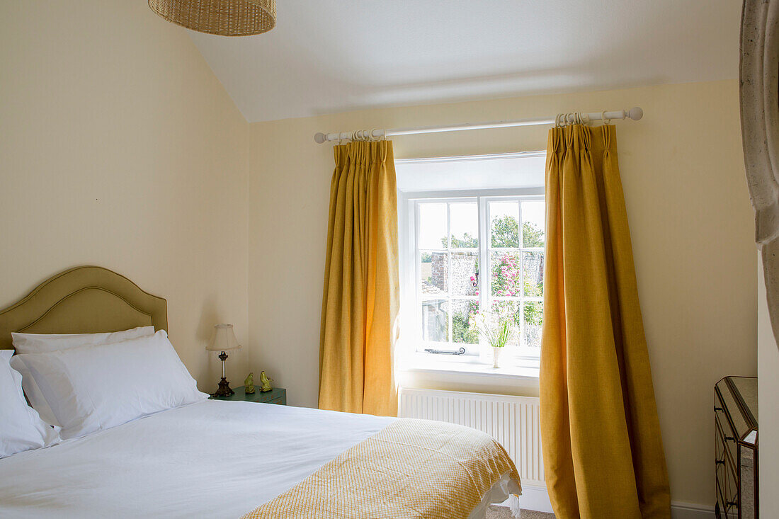 Weiße Bettdecke und Kissen auf einem Doppelbett mit gelben Vorhängen im Schlafzimmer eines Bauernhauses in Petworth, West Sussex, Kent