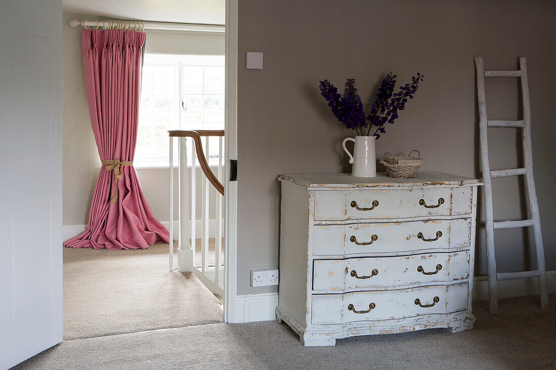 White chest of drawers with view to pink curtains at window on landing in Petworth farmhouse West Sussex Kent