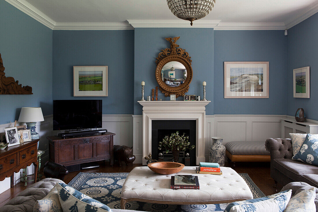 Convex mirror above fireplace with TV on side unit in light blue Amberley living room West Sussex England UK