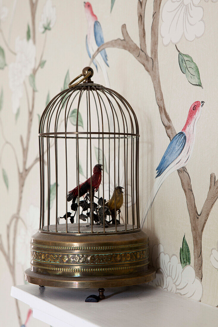 Birdcage on mantlepiece with patterned wallpaper in Amberley home West Sussex England UK
