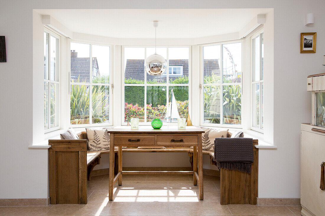 Holztisch und Sitzbank im Fenster eines Hauses in West Wittering, West Sussex, England