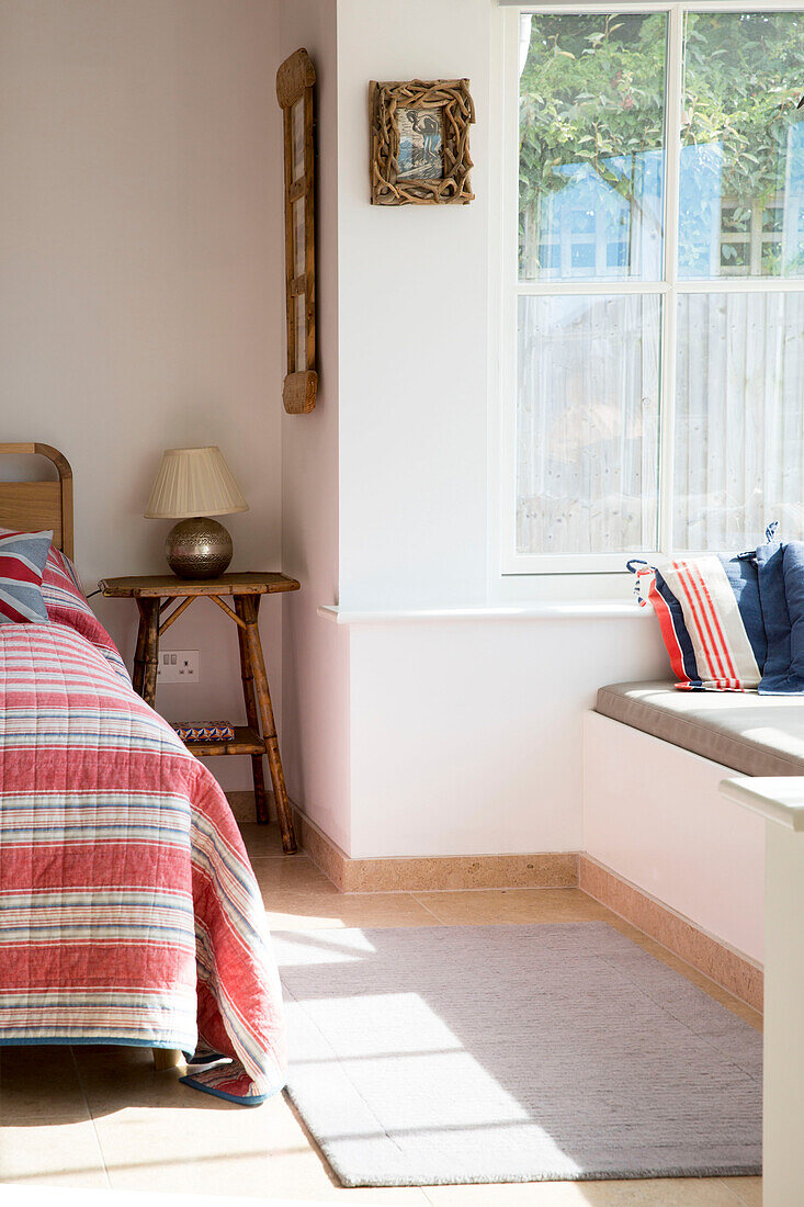 Window seat and rug with striped bed covers and lamp in West Wittering home West Sussex England