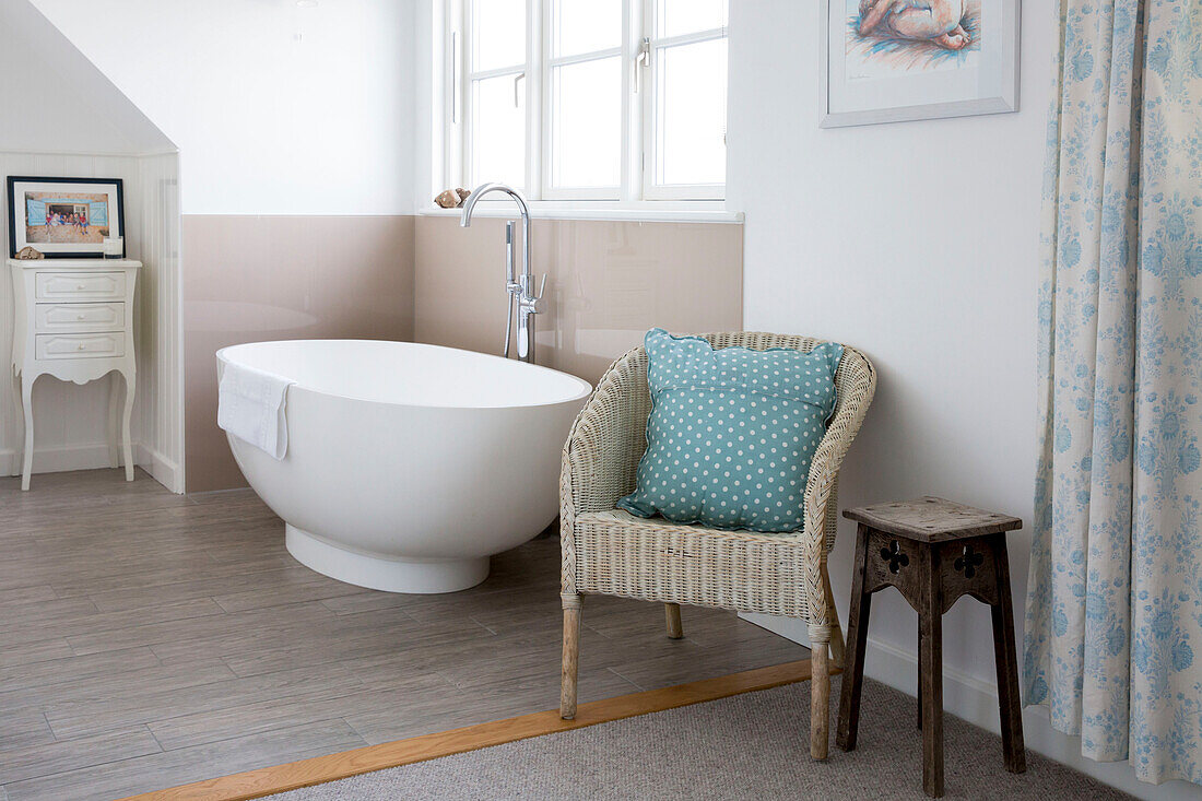 Spotty cushion on wicker chair with freestanding bath in West Wittering home West Sussex England