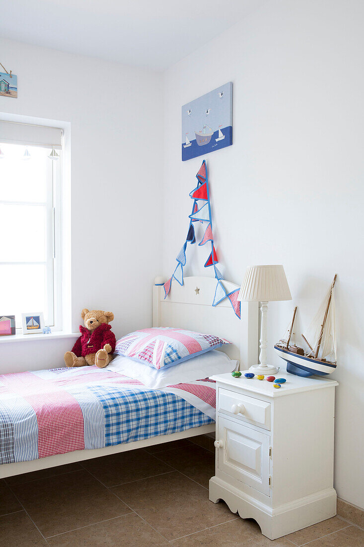Spielzeugboot und Teddybär mit Patchwork-Bettdecke auf Einzelbett in einem Haus in West Wittering, West Sussex, England
